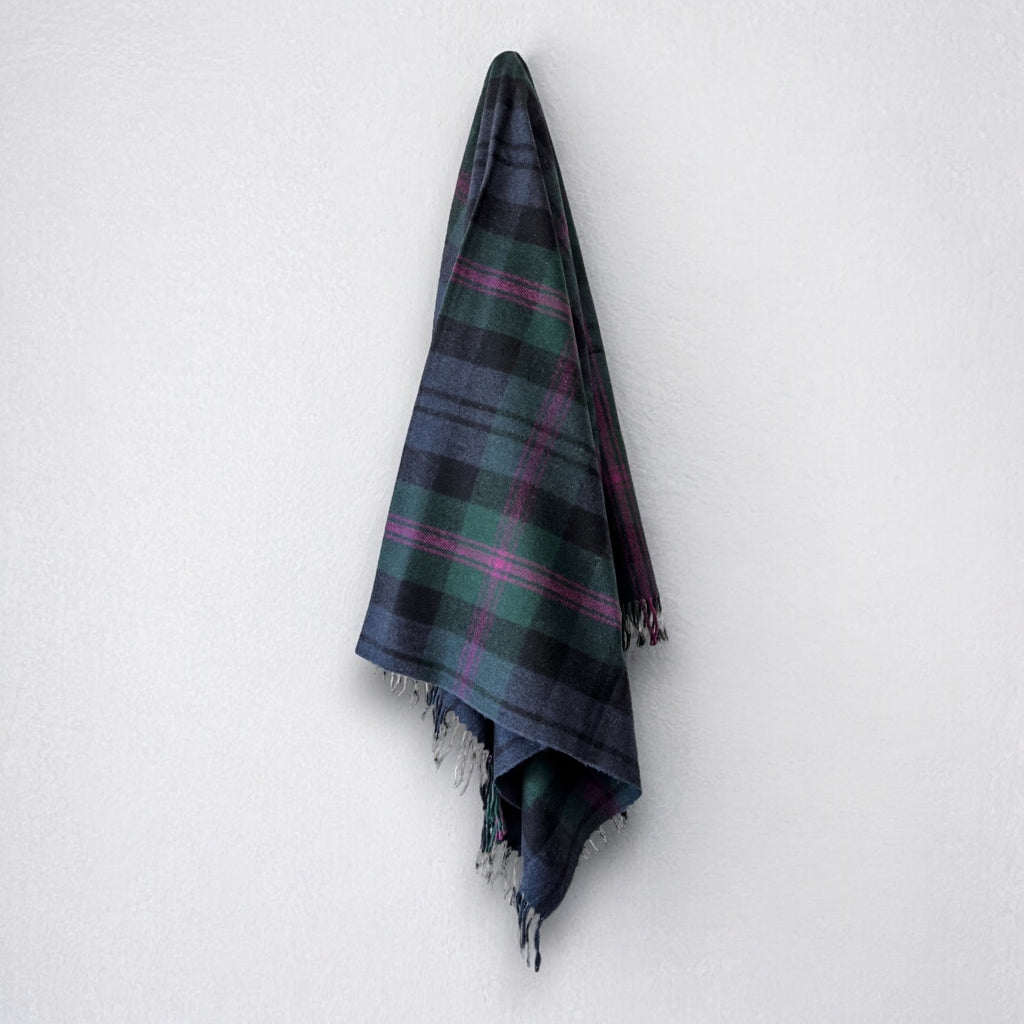 a 100% recycled blanket in baird tartan hanging from a wall hook on a white background 