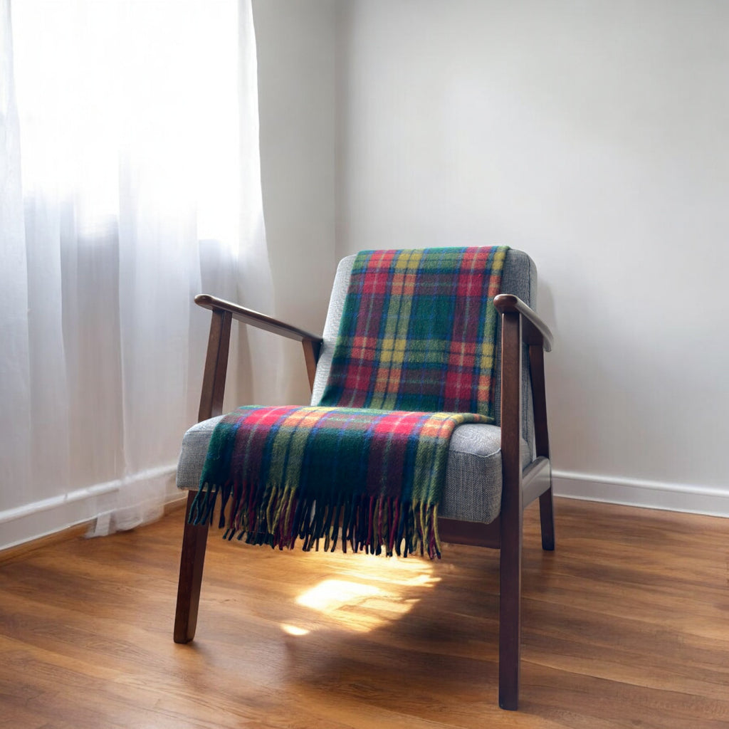 A buchanan modern recycled wool tartan knee blanket with fringed edges draped over a wooden chair in a room with a light interior.