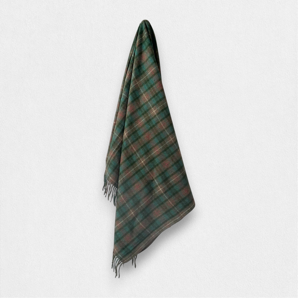 A dark green and brown tartan plaid scarf with fringed edges, hanging against a plain light gray background.