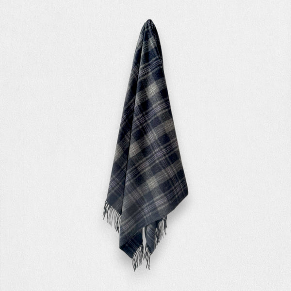 A 100% recycled wool dark navy and gray plaid scarf with fringed edges, hanging against a plain light gray background.
