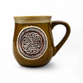 A stoneware mug with a Celtic circle pattern and a yellow enamel finish on the upper part.