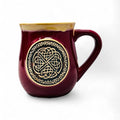 A red stoneware mug with a Celtic circle design in black.