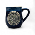 A blue stoneware mug with a Celtic circle design in the center.