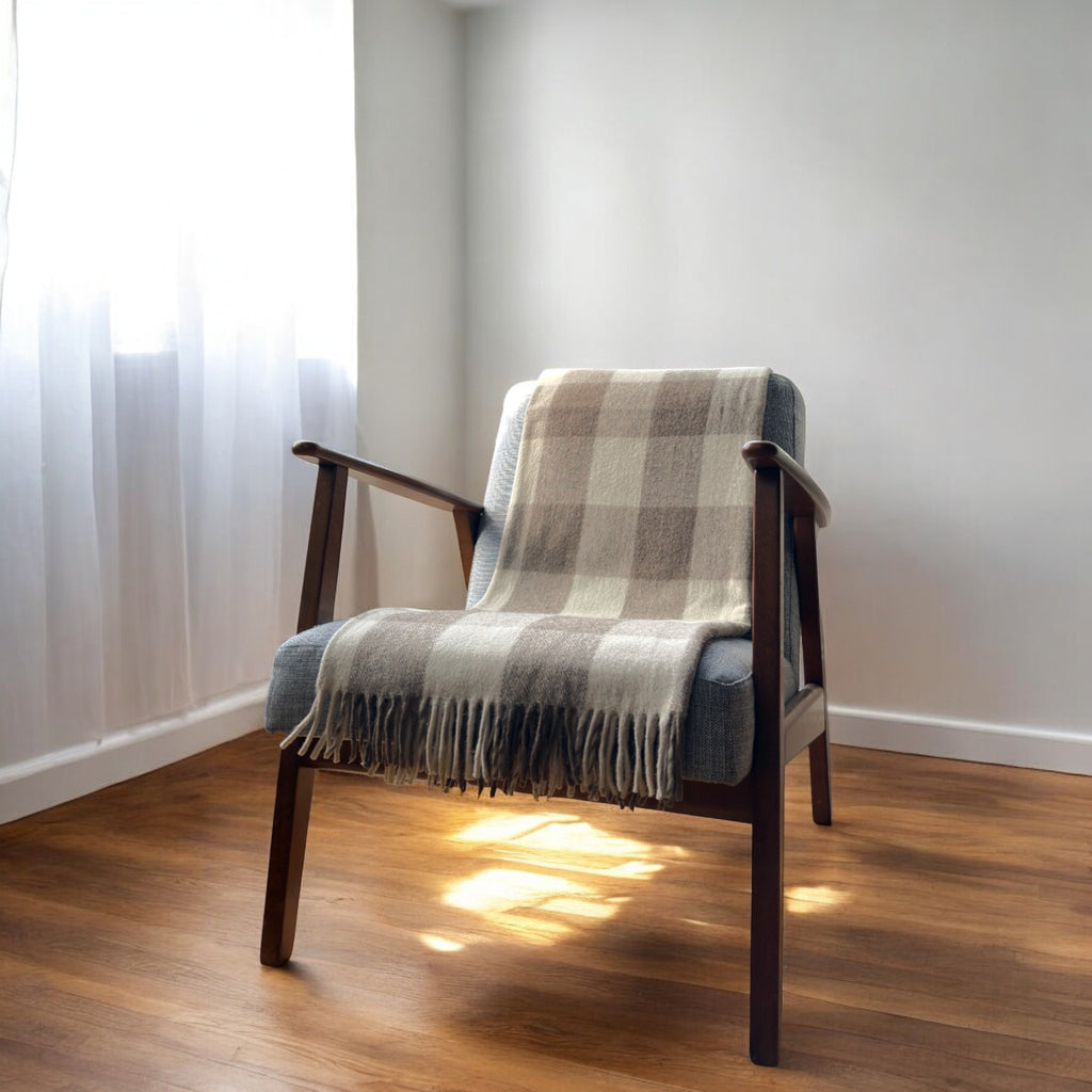 A jacob recycled wool tartan knee blanket with fringed edges draped over a wooden chair in a room with a light interior.