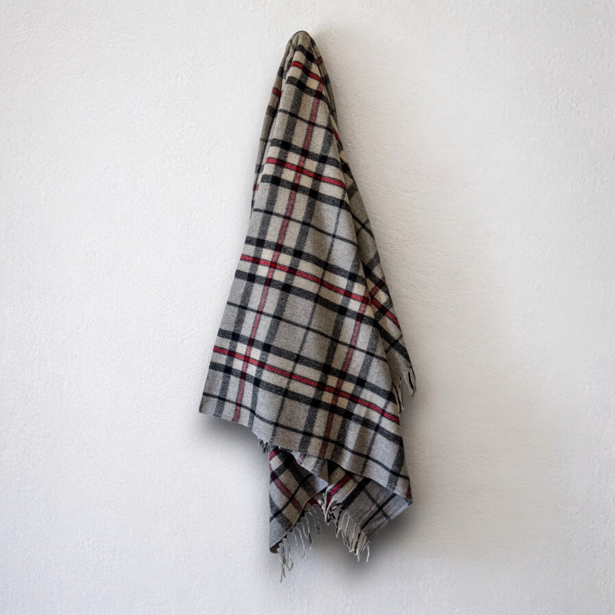 a 100% recycled blanket in thomson grey tartan hanging from a wall hook on a white background 