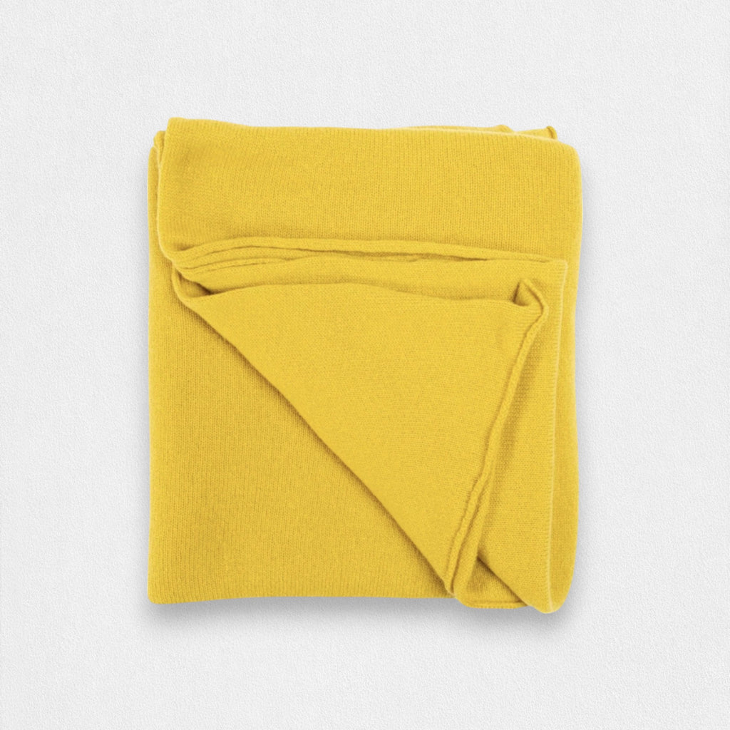 A folded mustard yellow cashmere wrap on a plain background.