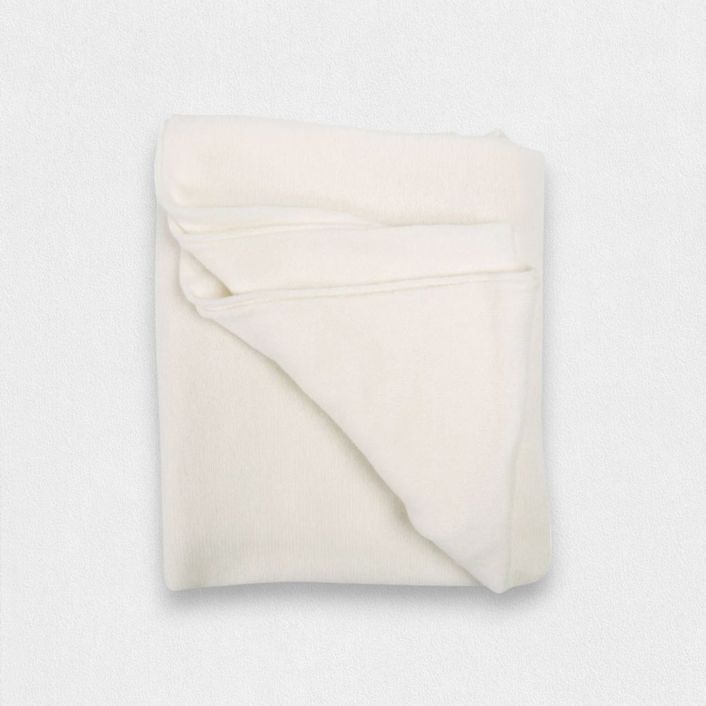 A folded white cashmere wrap on a plain background